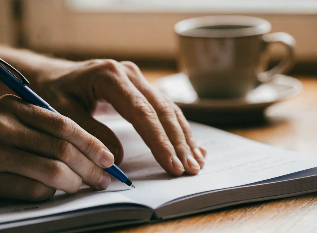 Mãos adultas respondendo à mão o caderno de provas sobre a mesa