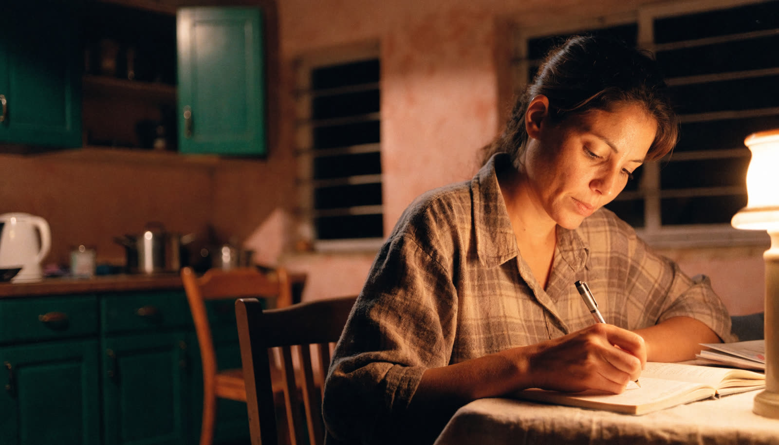 Mulher adulta estudando à noite, na mesa da cozinha de casa